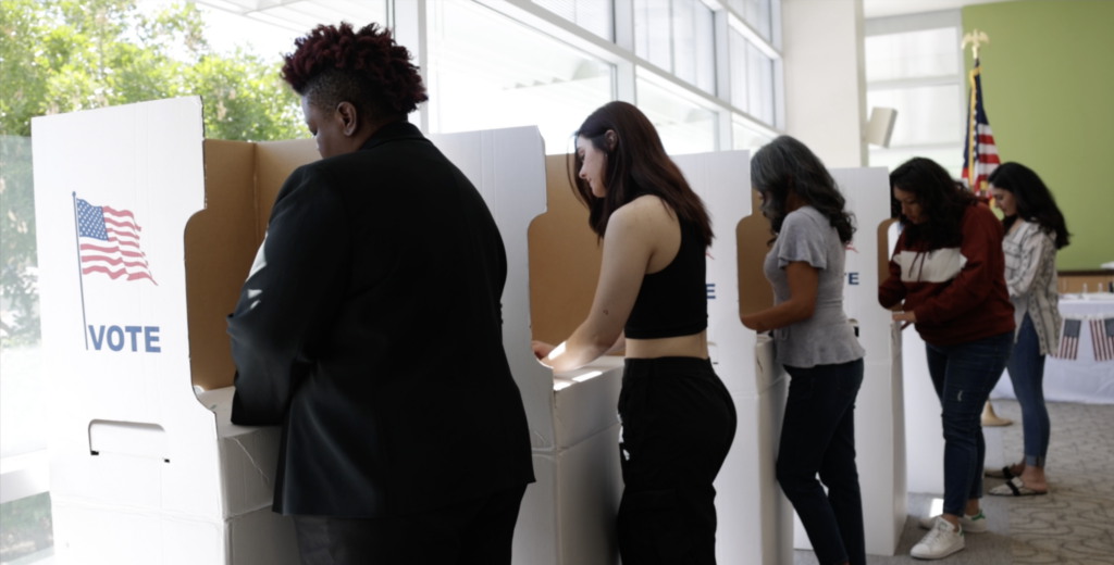 A photo depicting a diverse group of Americans voting in elections in private voting booths at a polling center.