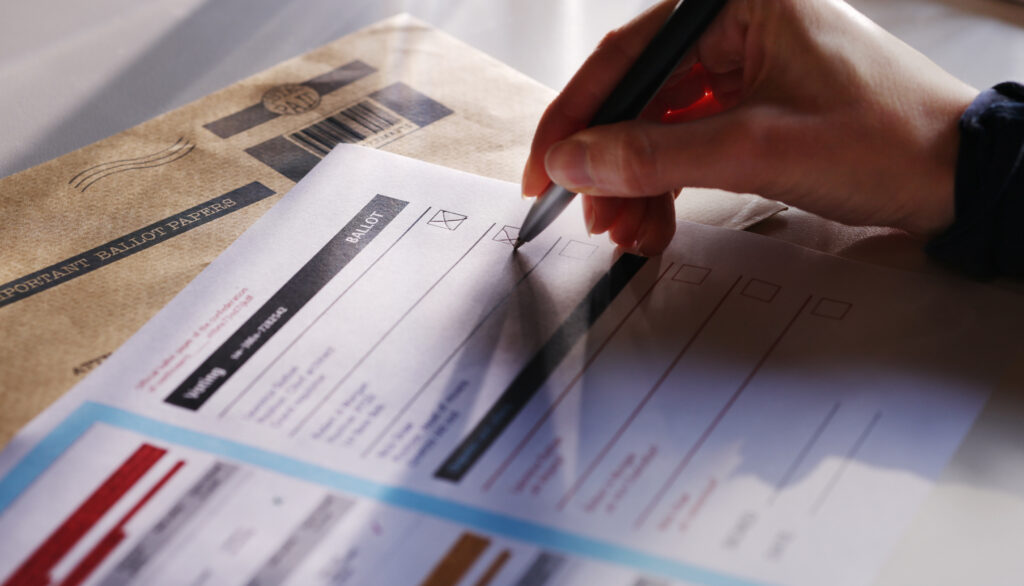 An image showing a hand filling in a blurred/shadowed ballot with a ballpoint pen.